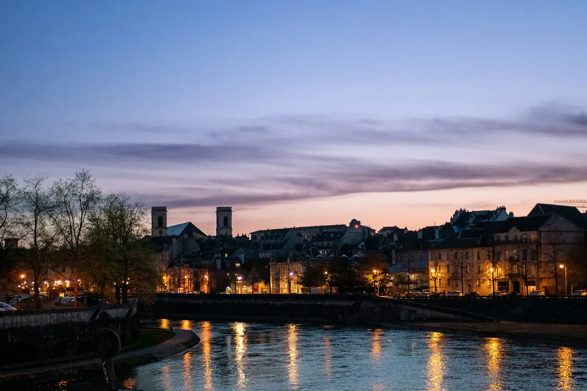 Les quais du Doubs à Besançon au crépuscule, lumières de la ville reflétées dans l’eau