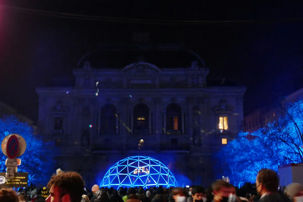 Foule devant un monument illuminé dans le centre de Lyon pendant la Fête des Lumières