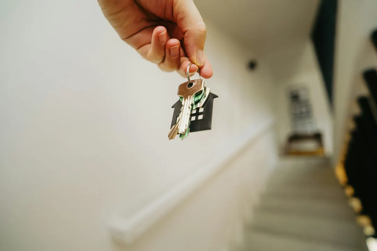Main tenant les clés d’un appartement devant un escalier